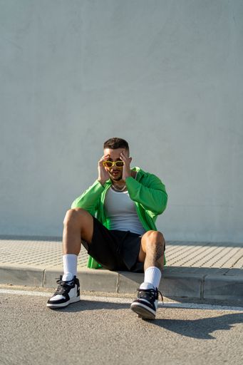 A Spanish bearded attractive young male sitting on the sidewalk posing in stylish clothes