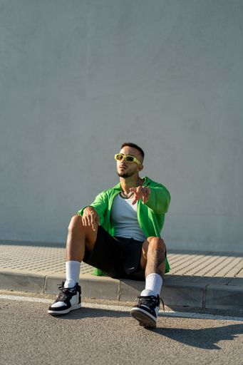 A Spanish bearded attractive young male sitting on the sidewalk posing in stylish clothes