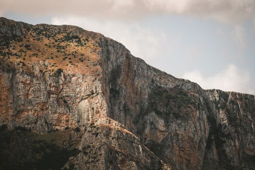 A rocky mountain with grass on it under the cloudy sky