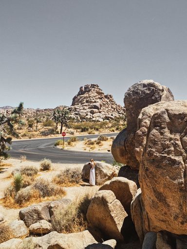 A beautiful vertical shot of a road with boulders and a woman on it during a hot summer day