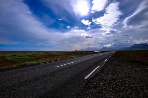 A beautiful shot of a road in the middle of a field with mountains in the distance under a cloudy sky