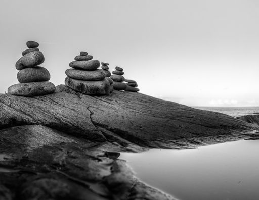 A grayscale shot of a peaceful lake with rocky coast and balanced pebbles' stacks