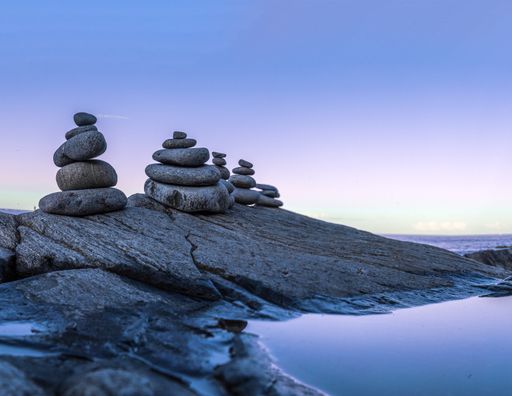 A peaceful lake with rocky coast and balanced pebbles' stacks under a blue clear sky