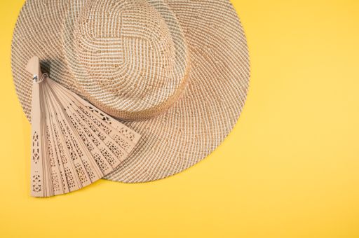 A round straw hat and a folding hand fan isolated on a yellow background with free space for text- concept for hot summer weather