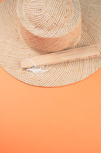 A round straw hat and a folding hand fan isolated on a peach background with free space for text- concept for hot summer weather