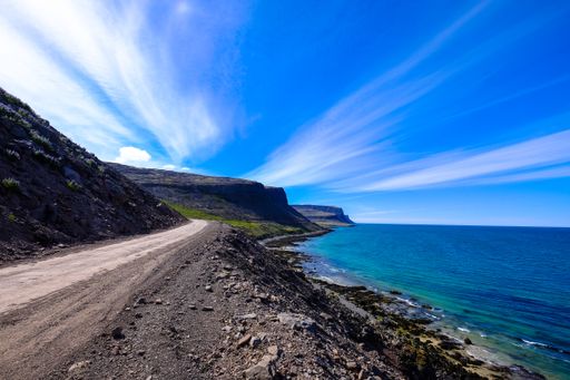 A dirt road in the middle of the hills near the sea under a blue sky