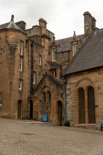 Historic stone building with arched windows and cobblestone path, showcasing architectural details under a cloudy sky.