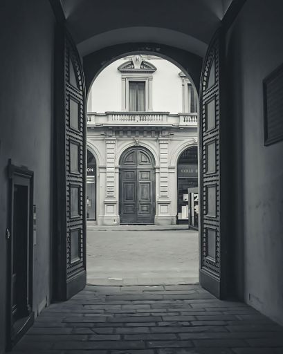 A monochrome view through an ornate doorway to a historic building facade in Florence, Italy.