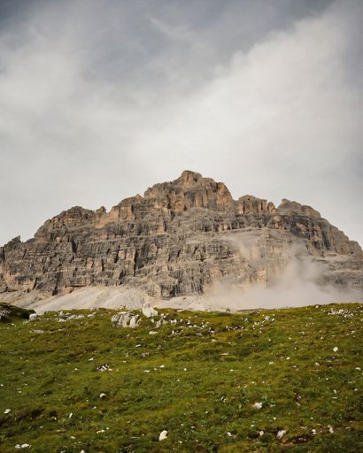 Majestic mountain peak against a cloudy sky with lush green foreground, capturing the serene beauty of nature.