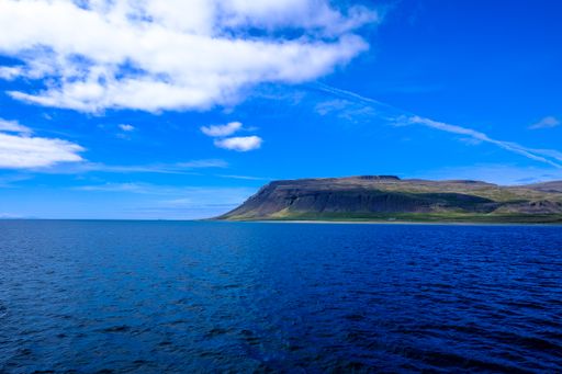 A beautiful shot of a sea with mountains in the distance under a blue cloudy sky