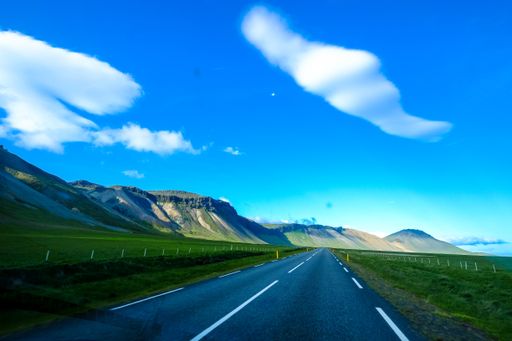A beautiful shot of a road in the middle of grassy fields with mountains on a side under a blue sky