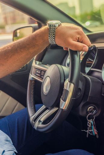 A vertical shot of a person holding a wheel and driving a car