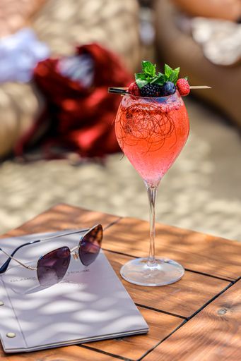 A vertical shot of a vibrant red drink placed outside on a wooden table with shadows falling on it