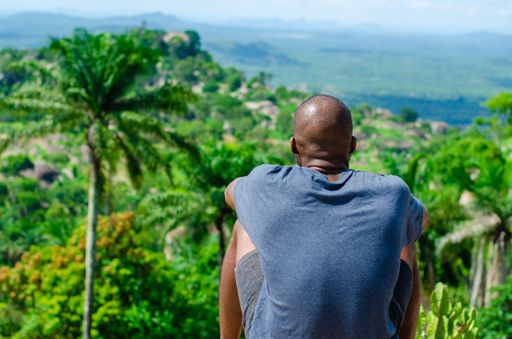 A closeup of an African man sitting with his back toward the camera and lush greenery in front of him