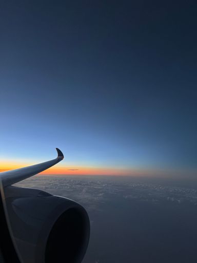View from airplane window at sunset with vibrant sky and wing silhouette.