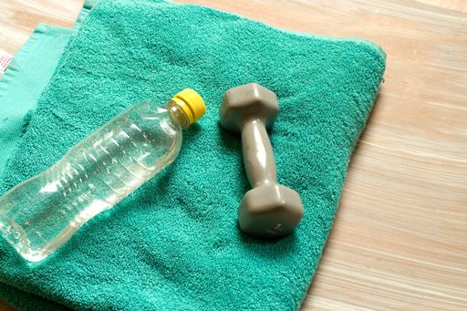 The blue dumbbells for fitness and a bottle of water on a blue towel on the floor