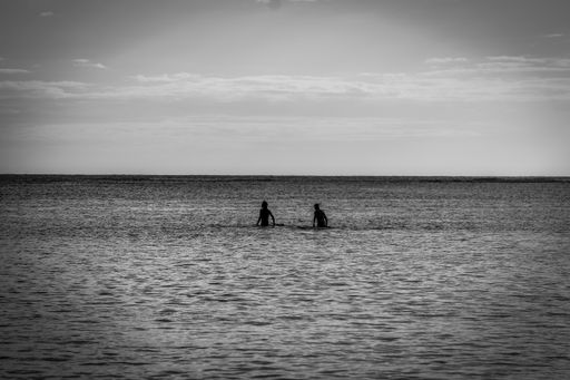 A silhouette of two people in the water in black and white