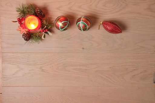 A candle and the Christmas tree toys on a wooden surface viewed from above