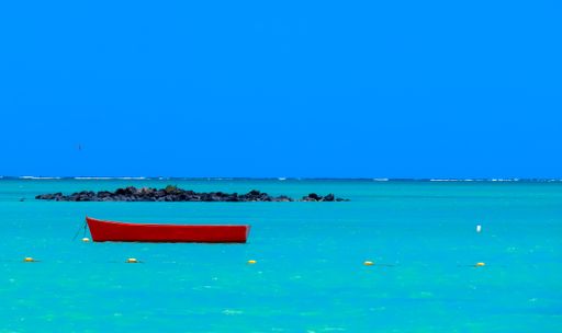 A beautiful shot of a red wooden boat resting on the water under a clear blue sky