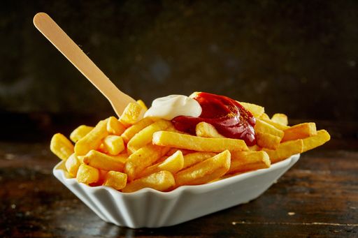 The appetizing French fries with mayo and ketchup in ceramic bowl with disposable stick on dark background
