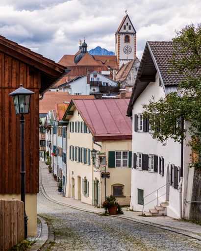 Charming street view in a European village with traditional houses and a church tower under a cloudy sky.