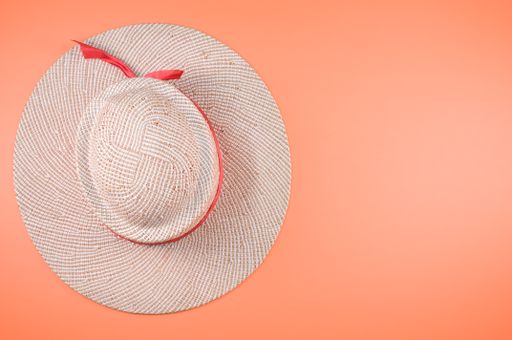 A top view of a straw hat with red ribbon isolated on an orange background