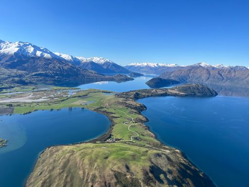 Aerial view of Lake Wanaka with snow-capped mountains and clear blue sky in New Zealand, showcasing stunning natural beauty.