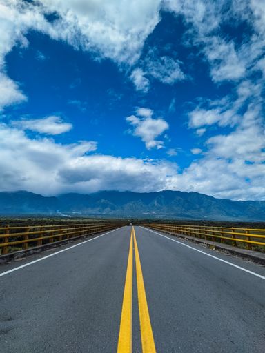 A vertical shot of an empty road to hills on a cloudy day