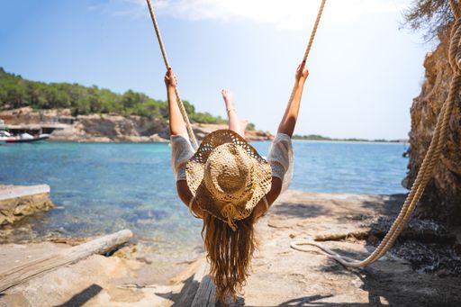 Girl with a straw hat swinging on a rope in front of the sea on a sunny summer day