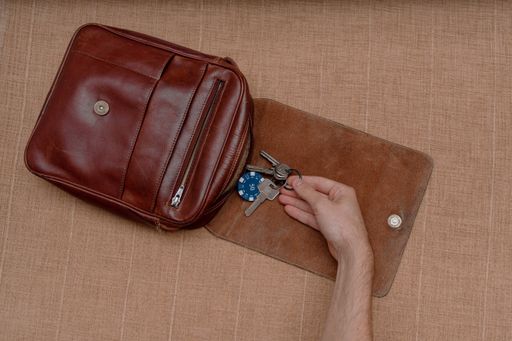 A top view shot of a person taking out keys from a leather brown men's bag