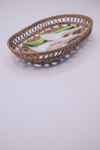 A vertical shot of plastic fork and spoon on a wicker basket isolated on light gray background