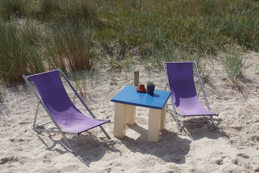 A bright summer day at the beach with two chairs set up next to a small table next to tall grass