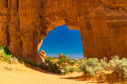Scenic view through a natural rock arch in Arches National Park, Utah, with vibrant blue sky and desert landscape.