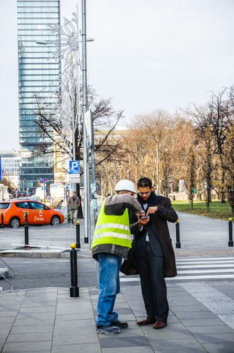 A construction worker and a businessman looking at a smartphone in the city center