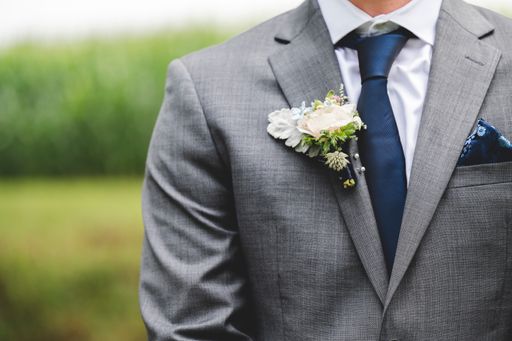 A closeup shot of a groom wearing a grey tuxedo in a venue in nature