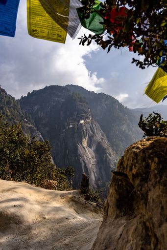 Scenic view of Tiger's Nest Monastery in Bhutan with colorful prayer flags under a partly cloudy sky.