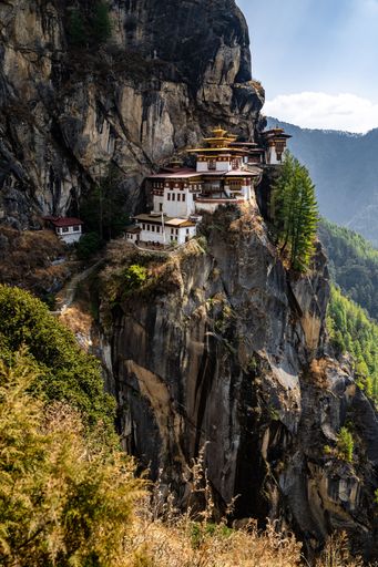 The iconic Paro Taktsang monastery perched on a cliffside in Bhutan, surrounded by lush greenery and rugged mountains under a clear sky.