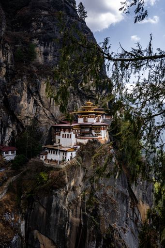 Tiger's Nest Monastery perched on a cliffside in Bhutan, surrounded by lush forest and rugged mountains under a partly cloudy sky.