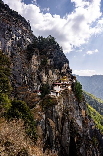 Tiger's Nest Monastery perched on a cliff in Bhutan with stunning mountain views and a partly cloudy sky.