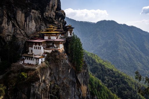 The iconic Tiger's Nest Monastery perched on a cliff in Bhutan, surrounded by lush green mountains under a clear blue sky.