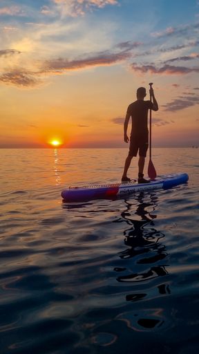 A vertical shot of a man on a paddleboard in Barcelona, Spain during sunset