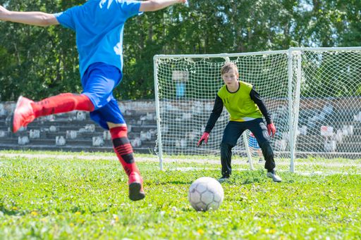 The young football goalkeeper is ready to throw, and the field player in the jump strikes at the goal.