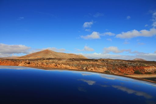 A beautiful shot of sea near deserted hills and mountains in the distance under a blue sky