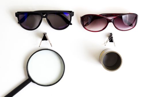 The two sunglasses and a magnifier on a white surface viewed from above