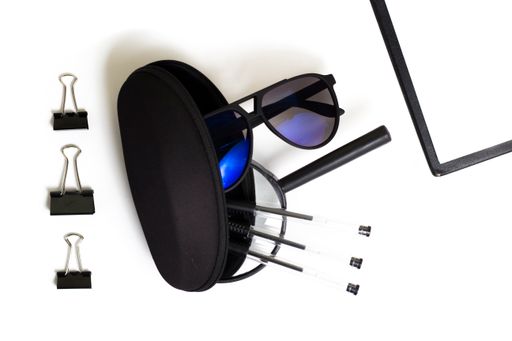 A sunglass, notepad and clips on a white surface viewed from above