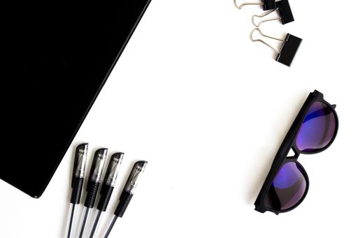 A magnifier, notepad and sunglasses on a white surface viewed from above