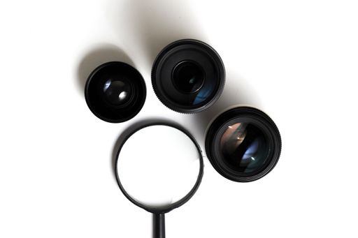 A magnifier and photo camera lenses on a white surface viewed from above