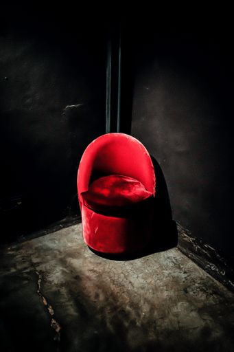 A vertical shot of a red suede chair in the corner of black walls