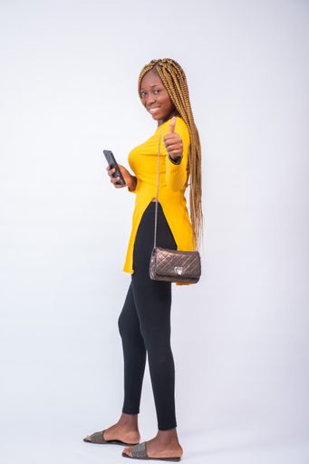 A beautiful African lady using her phone with a smile on her face, standing against a white background