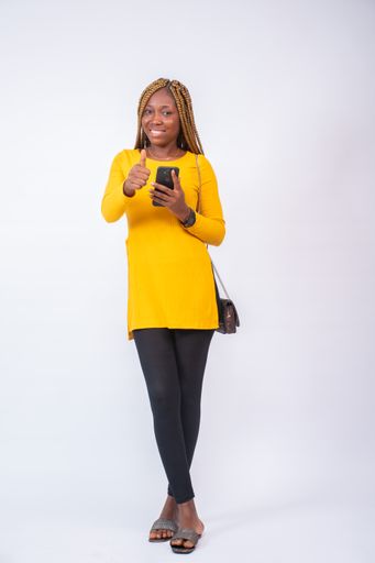 A beautiful African lady using her phone, with a smile on her face, standing against a white background